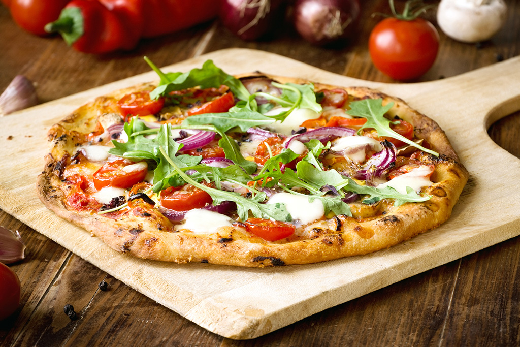 Freshly baked homemade pizza topped with arugula, tomatoes, red onions, and melted cheese on a wooden board.